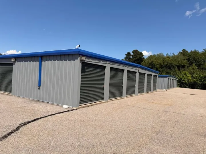 Rows of drive-up storage units in Coventry, RI, with green roll-up doors under a blue sky near a treeline