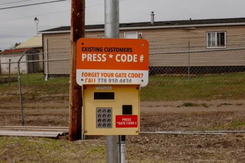 An electronic gate keypad with instructions for existing customers to enter their gate code under an orange sign