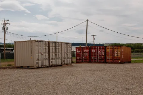 Outdoor gravel storage lot featuring rows of tan and red metal shipping containers under power lines