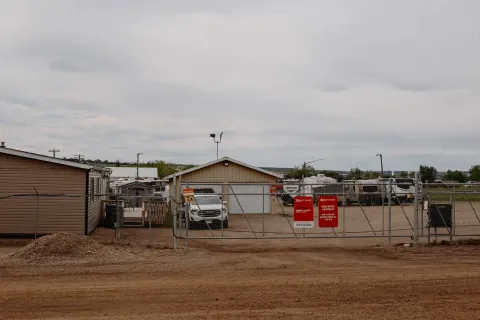 A chain-link gate with red signage provides access to a gravel storage lot for vehicles and RVs