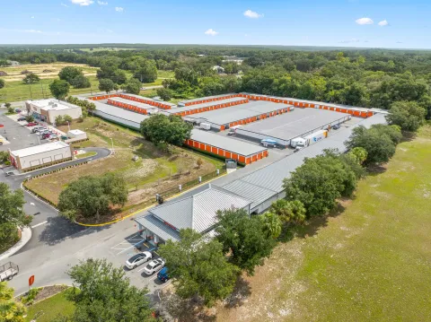 Aerial view of a self-storage facility with several buildings featuring orange unit doors and grey roofs