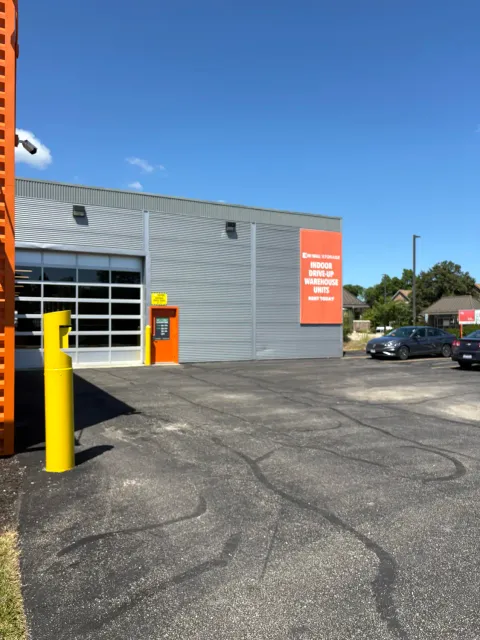 Storage facility exterior with a large glass bay door, orange personnel door, and paved parking lot