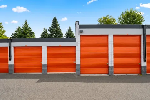 Four orange roll-up storage unit doors with white trim and grey brick accents under a blue sky