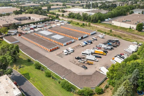 Aerial view of several storage buildings with orange doors and a parking lot for trucks and trailers