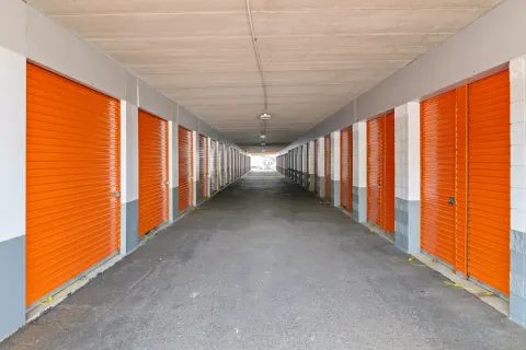 Long covered driveway lined with orange roll-up storage unit doors under a white concrete ceiling
