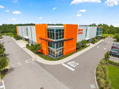 Exterior view of a multi-story storage building with orange panels and glass windows next to a road