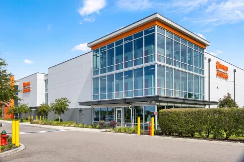 Modern multi-story self-storage building with a large glass facade, orange accents, and a paved parking lot