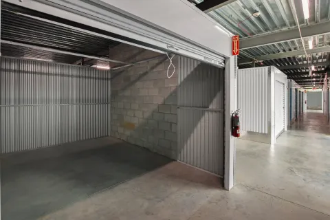 Empty indoor storage unit with corrugated metal walls, a concrete floor, and a fire extinguisher mounted outside