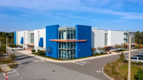 Multi-story storage facility with blue and white exterior walls, glass corners, and orange awnings along a driveway