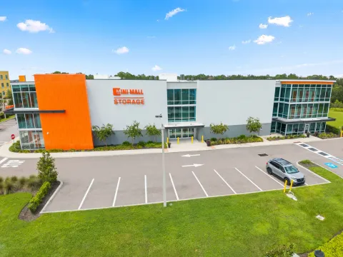 Exterior of a multi-story Mini Mall Storage facility with orange accents, glass windows, and a parking lot