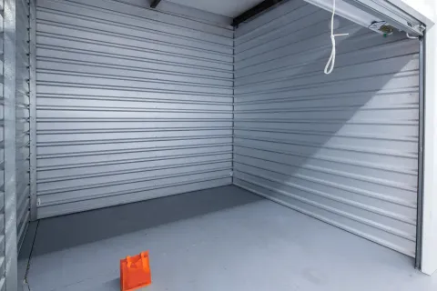 Interior view of an empty storage unit with corrugated metal walls and an orange bag on the floor