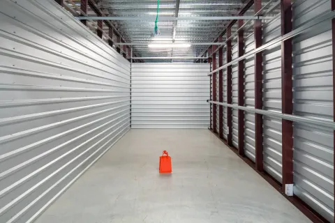 Empty self-storage unit with metal walls, a concrete floor, and one small orange bag in the center