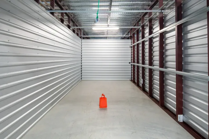 Empty self-storage unit with metal walls, a concrete floor, and one small orange bag in the center