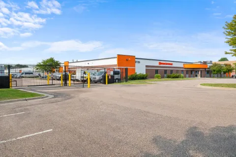 Exterior view of a self-storage facility with orange accents and a gated parking area for vehicles