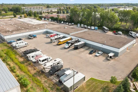 Aerial view of an outdoor paved storage lot with parked RVs, boats, trailers, and a school bus