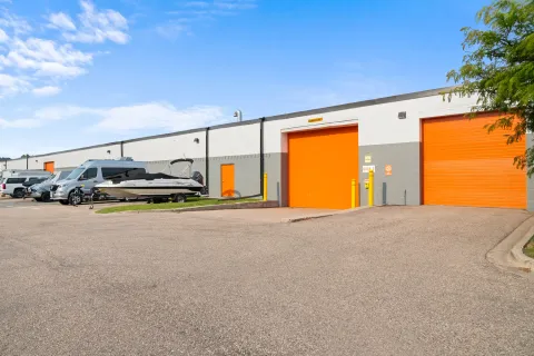 Building exterior with large orange roll-up doors, a boat on a trailer, and a silver van