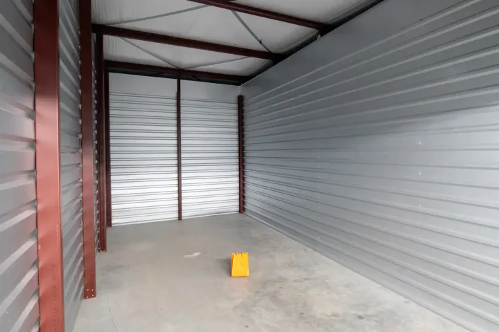 An empty drive-up self-storage unit featuring corrugated metal walls, a concrete floor, and high ceilings