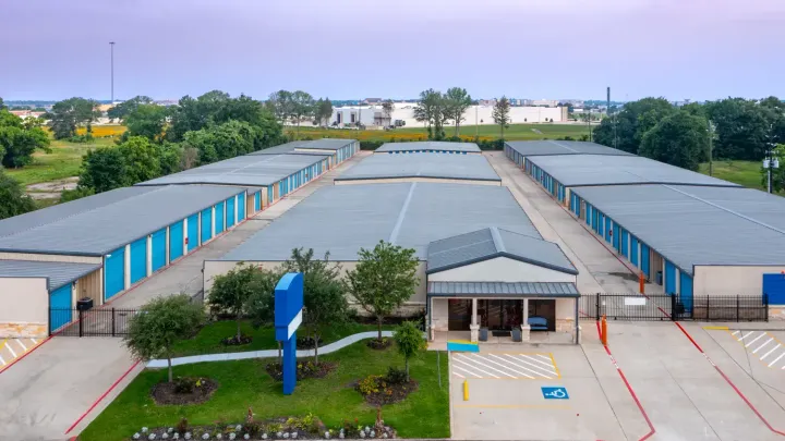 An aerial view of a self-storage facility featuring rows of blue units and an office building