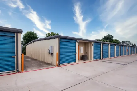 Outdoor drive-up self-storage facility with tan metal siding and blue roll-up unit doors along a concrete path