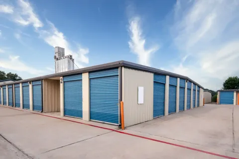 Exterior view of a self-storage building with blue roll-up doors and a concrete drive-up aisle