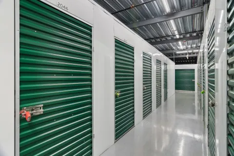 Indoor storage hallway with white walls, polished gray floors, and rows of green roll-up unit doors