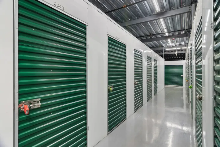 Indoor storage hallway with white walls, polished gray floors, and rows of green roll-up unit doors