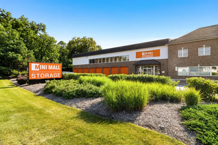 A brick Mini Mall Storage facility with orange doors, landscaped bushes, and a large monument sign