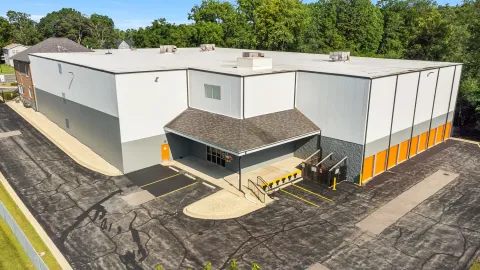 High-angle view of a white multi-story storage building with orange unit doors and an office entrance