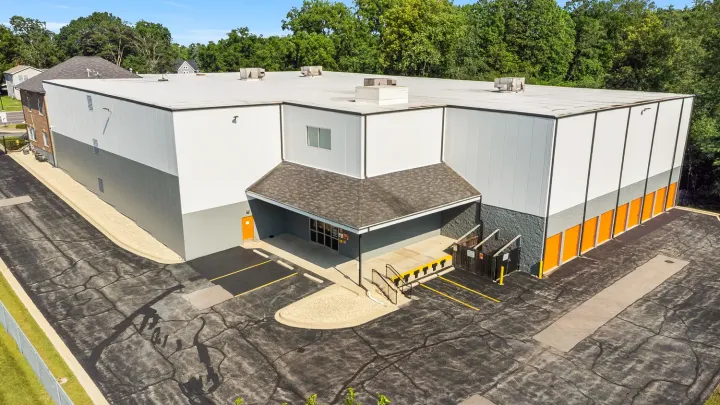 High-angle view of a white multi-story storage building with orange unit doors and an office entrance