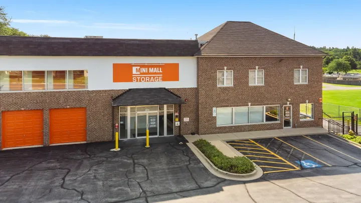 A brick building with an orange Mini Mall Storage sign, glass entrance, and paved parking lot