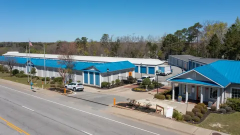 High-angle view of a self-storage facility with blue roofs, drive-up units, and a gated entrance office