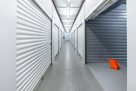 An indoor storage hallway with white roll-up unit doors and an orange bag on the floor