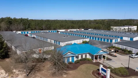 Aerial view of a storage facility featuring a blue-roofed office building and several long rows of units