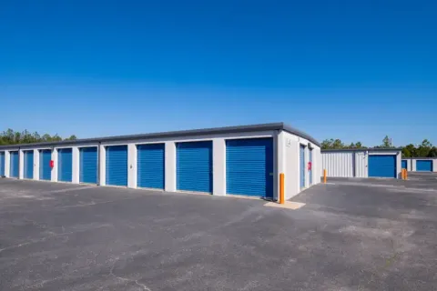 Rows of outdoor drive-up storage units with blue roll-up doors under a clear sky