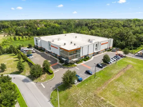 Aerial view of a multi-story self-storage facility with a glass office corner and paved parking lot