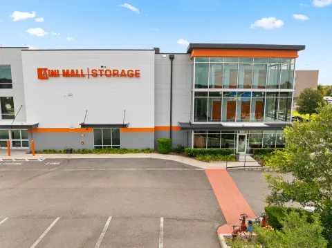 Modern Mini Mall Storage facility exterior with multi-story glass windows, orange trim, and paved parking lot
