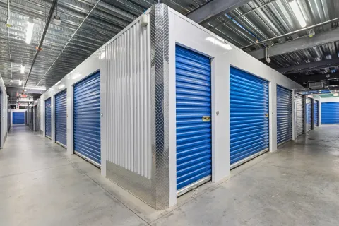 Interior hallway of a storage facility featuring blue roll-up doors and diamond plate corner guards