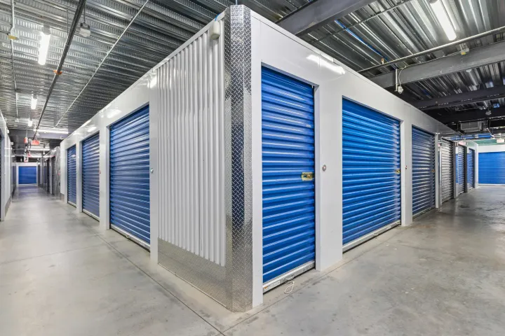 Interior hallway of a storage facility featuring blue roll-up doors and diamond plate corner guards