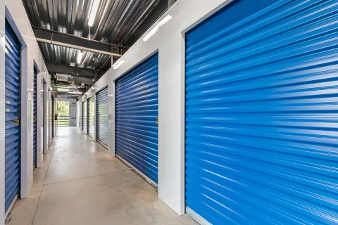 Indoor storage hallway featuring a row of blue corrugated metal roll-up doors and white walls