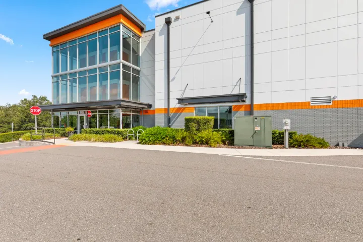 Exterior of a multi-story storage facility with large glass windows, orange trim, and a paved parking area