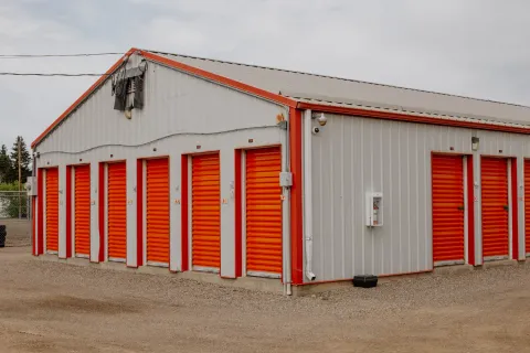 Exterior view of a metal self-storage building with orange roll-up doors and a gravel driveway
