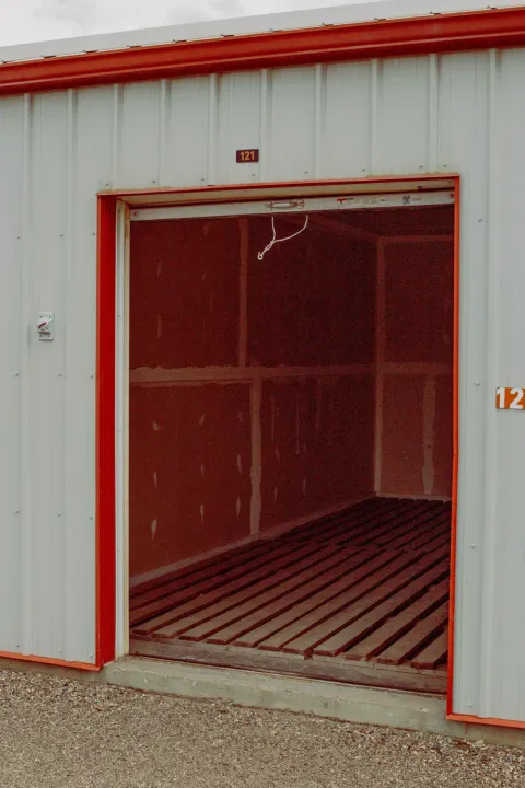 An open drive-up storage unit with a red door frame and a wooden pallet floor interior