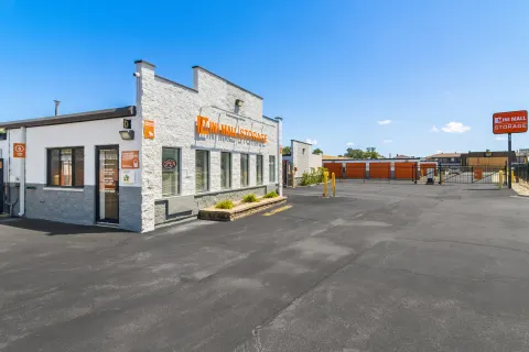 Mini Mall Storage rental office exterior with asphalt parking lot and gated drive-up orange storage units