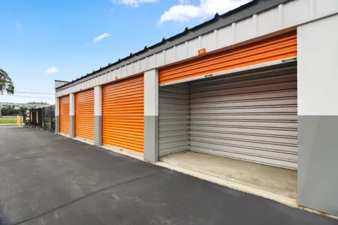 Row of drive-up storage units with orange roll-up doors and one open unit showing the interior