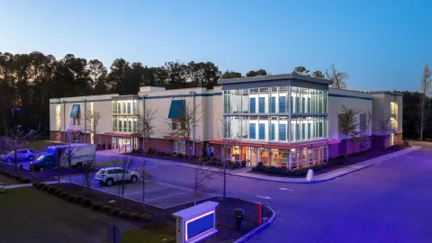Modern multi-story self-storage facility with glass windows showing interior blue unit doors at dusk