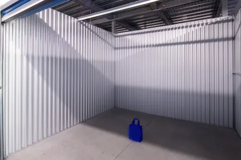 Interior view of an empty storage unit with corrugated metal walls and a single blue bag