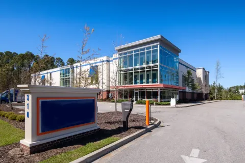 A multi-story storage building with a glass storefront office located behind a blue monument sign