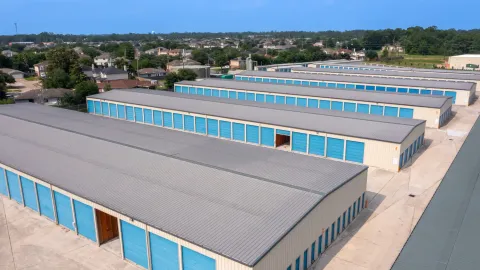 Aerial view of long rows of drive-up storage buildings with blue roll-up doors and gray metal roofs