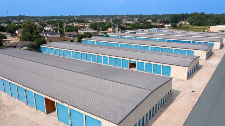 Aerial view of long rows of drive-up storage buildings with blue roll-up doors and gray metal roofs