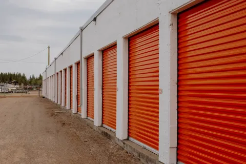 Row of drive-up self-storage units with orange roll-up doors and a white exterior wall